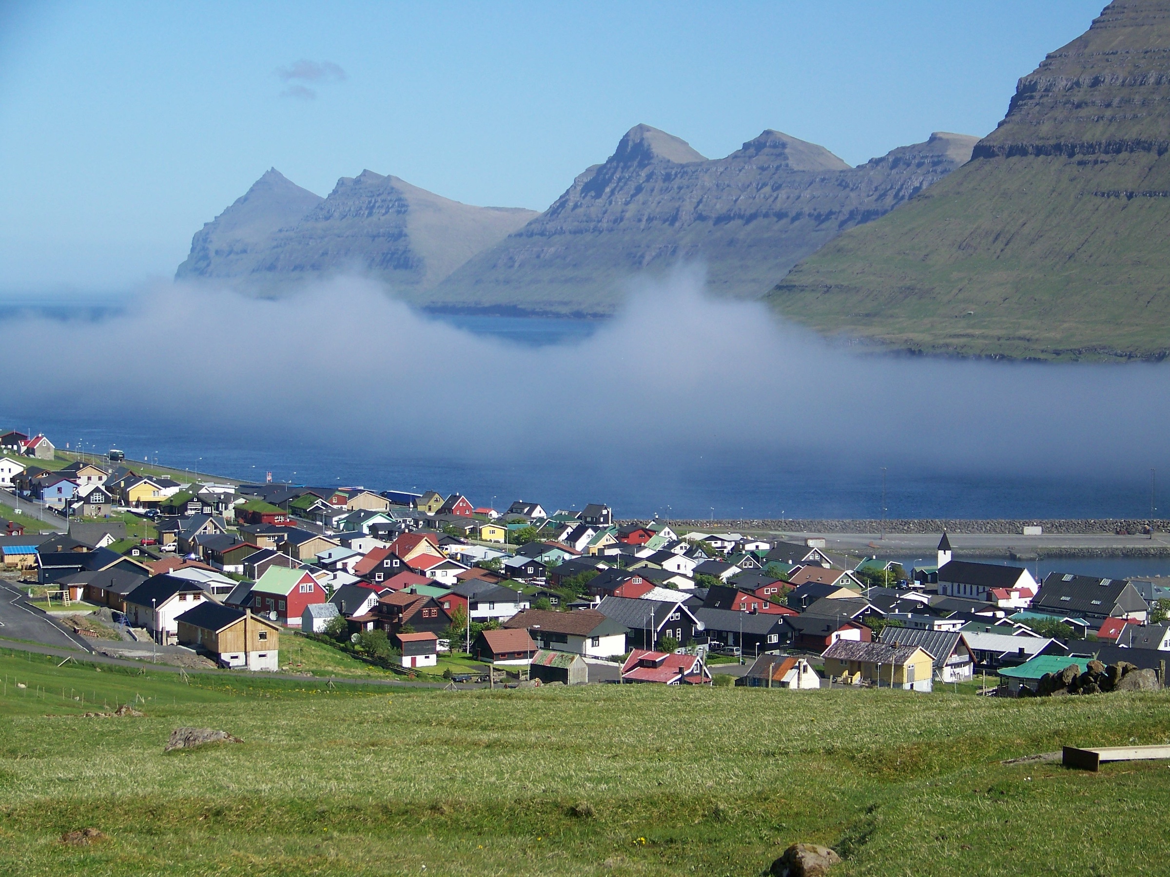 Ein Dorf an einem Fjord der Färöer. Wer die Überfahrt in Tórshavn unterbricht, sieht auf den Inseln solche Ausblicke.